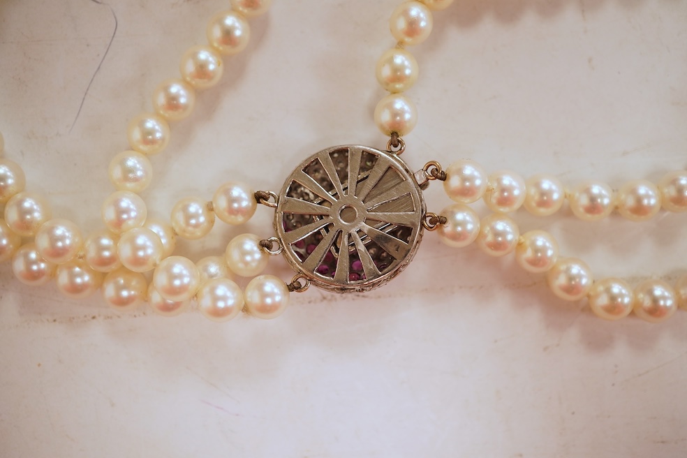 A cultured pearl, ruby and diamond clasp, composed of three rows of cultured pearls measuring approximately 6.9mm diameter, to a white precious metal (tests as 14k) disc-shaped clasp pavé-set with brilliant-cut diamonds